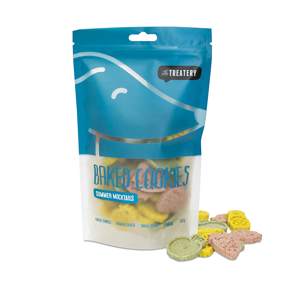 A package of 'Summer Mocktails' dog treats by The Treatery, featuring a blue and white bag with images of the cookie treats inside. The cookies appear to be in various shapes and colors, resembling tropical themes such as pineapples and leaves.
